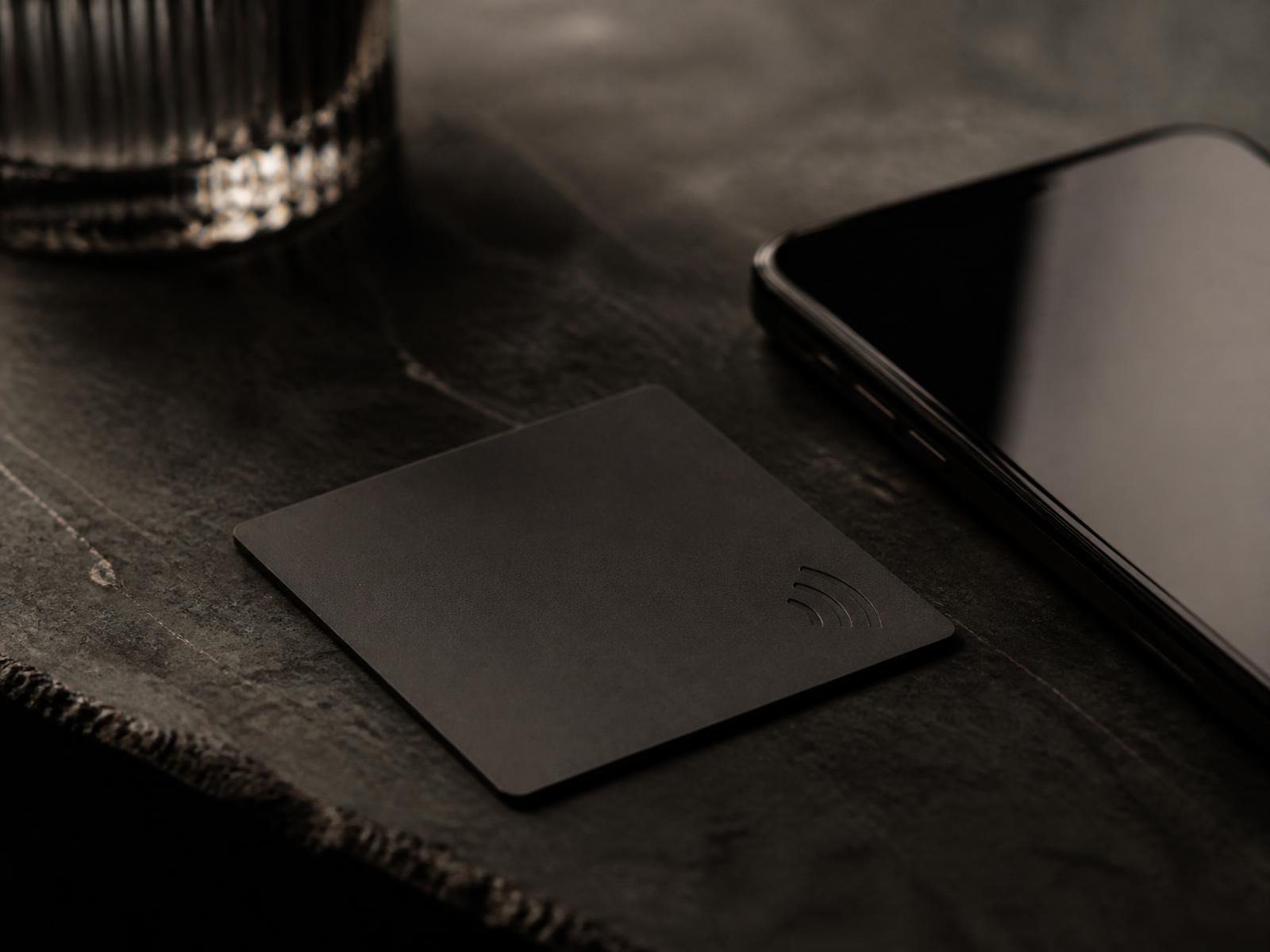 A matte black NFC card on a dark stone bar top beside a phone